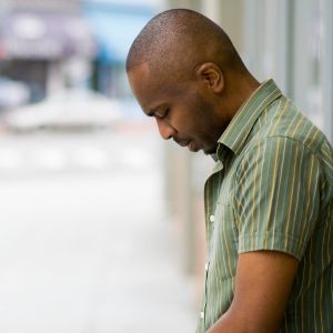 Man with a green striped short-sleeve shirt looking down on a sidewalk outdoors side profile