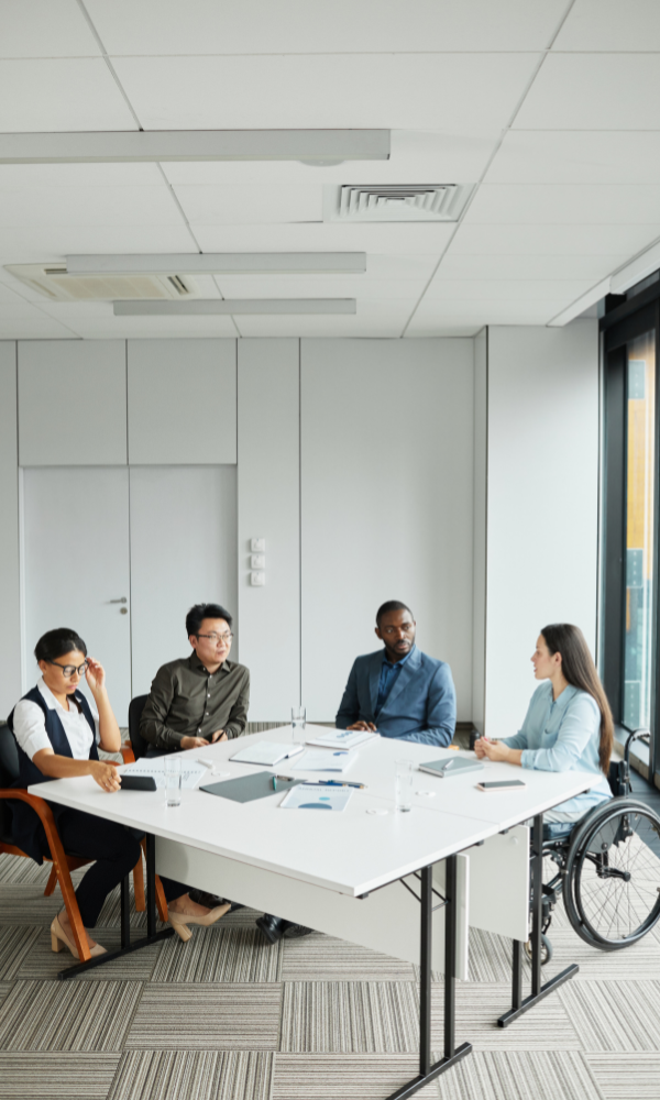 work colleagues and woman in wheel chair sitting at conference table